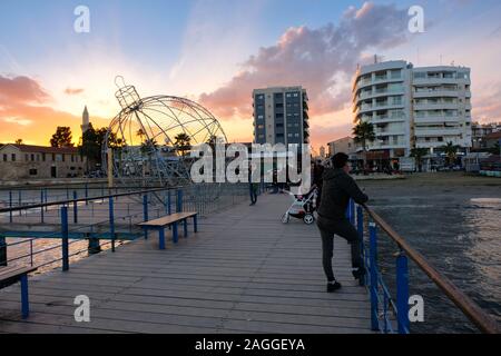 Larnaca, Zypern - 2. Januar 2018: Menschen auf der Pier bei Sonnenuntergang in Larnaca während der Ferienzeit. Blick Richtung Finikoudes Beach und Larnaca Castle. Stockfoto