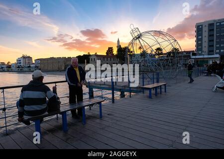 Larnaca, Zypern - 2. Januar 2018: Menschen auf der Pier bei Sonnenuntergang in Larnaca während der Ferienzeit. Blick Richtung Finikoudes Beach und Larnaca Castle. Stockfoto