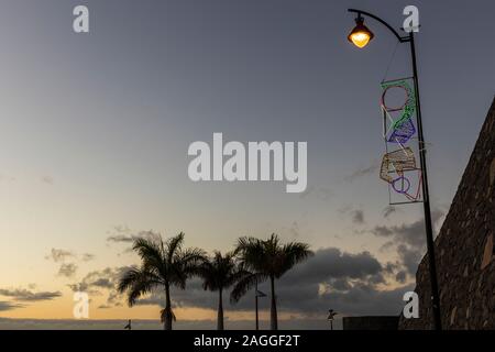 Weihnachten Dekoration leuchten auf einem lampost und einige Palmen bei Sonnenuntergang in Los Gigantes, Teneriffa, Kanarische Inseln, Spanien Stockfoto