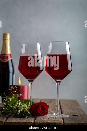 Zwei Gläser Wein und rote Rose mit brennenden Kerze und Flasche im Hintergrund auf rustikalen Holztisch Stockfoto