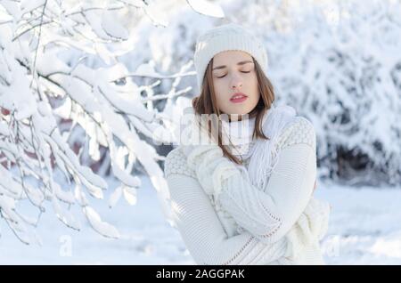 Ein Mädchen der kaukasischen Abstammung trägt einen weißen Pullover und Handschuhe an einem kalten Wintertag. Sie umarmen sich von der Kälte. Stockfoto