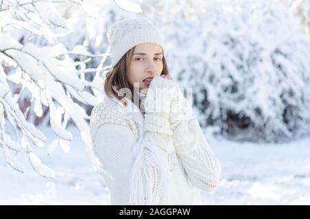 Eine kaukasische Mädchen trägt einen weißen Pullover und Handschuhe an einem kalten Wintertag. Sie wärmt Ihre Hände mit ihrem Atem, der aus der Kälte eingefroren sind. Stockfoto