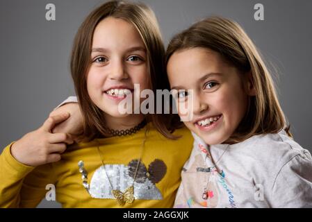 Identische Zwillinge Schwestern sind posieren für die Kamera. Happy Zwillingsschwestern in die Kamera schaut, lachen, lächeln, umarmen, halten sich an den Händen. Professio Stockfoto