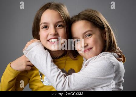 Identische Zwillinge Schwestern sind posieren für die Kamera. Happy Zwillingsschwestern in die Kamera schaut, lachen, lächeln, umarmen, halten sich an den Händen. Professio Stockfoto