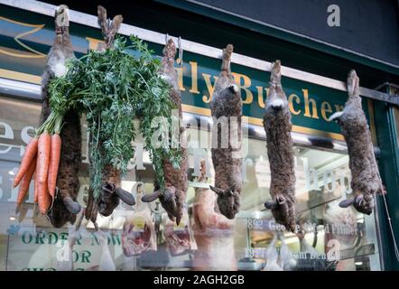 Tote Kaninchen zum Verkauf, zum Aufhängen von außerhalb ein Metzger Schaufenster Stockfoto