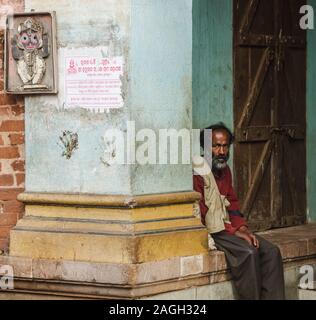 Bhubaneshwar, Orissa, Indien - 12. Februar 2018: Porträt eines Mannes, der neben einer Säule auf einer Bank außerhalb eines alten Hauses sitzt. Stockfoto