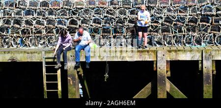 Gegangen angeln - Fischen mit der Hand Linien auf der Pier am Dock Ende, Whitby, Yorkshire, UK mit Krabben Töpfe hinter (2017) Stockfoto