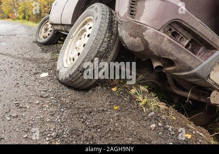 Ein Auto bei einem Unfall liegt in einem Graben durch die ländliche Straße tagsüber, bis Foto und das Rad in der Nähe des Stoßfängers hinten Stockfoto