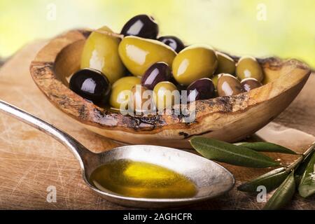 Auf der rustikalen Holztisch, eine Schüssel mit verschiedenen Arten von Oliven und einen Löffel voll mit Öl Stockfoto
