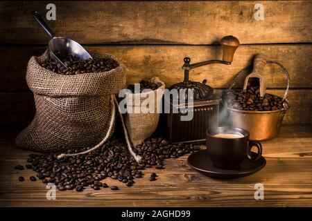 Kaffeebohnen in Jute Sack mit Holz Grinder und einer Tasse Kaffee Stockfoto