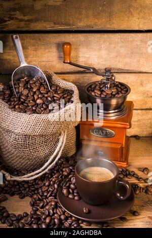 Kaffeebohnen in Jute Sack mit Holz Grinder und einer Tasse Kaffee Stockfoto