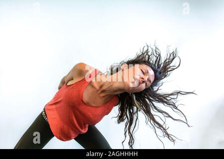 Eine gesunde und sportliche Frau ist von vorne gegen eine weiße Wand gesehen, mit langen Flippen brünette Haare, heiß und verschwitzt während erweiterter Fluss yoga Stockfoto