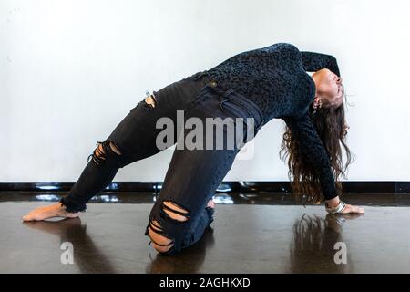 Eine Nahaufnahme von einem athletischen und Gymnastik für Erwachsene Frau in zerrissenen Jeans und floral bedrucktes Shirt, Übergang durch fortgeschrittene Yoga bewegt Stockfoto