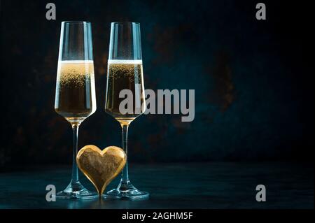 Zwei elegante romantische Brille mit funkelnden goldenen Champagner mit goldenen Herzen gegen einen dunkelblauen Hintergrund Stockfoto