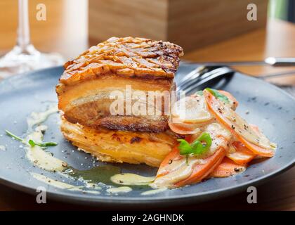 Frisch gegrillter Schweinebauch mit knusprigen Knistern mit glasierten Karotten und Kartoffeln musaka in einem Restaurant serviert, vergoldet Stockfoto