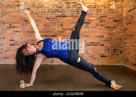 Eine schlanke kaukasische Frau gesehen wird durch erweiterte Yoga-stellungen während einer geistigen Strömung routine Übergang, das Tragen von Jeans und schimmernden Top Stockfoto