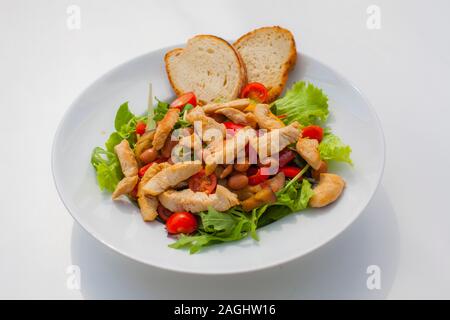 Teile von Hühnern auf Salat mit Tomaten und Bohnen gemischt und mit Brot auf dem Teller dekoriert Stockfoto