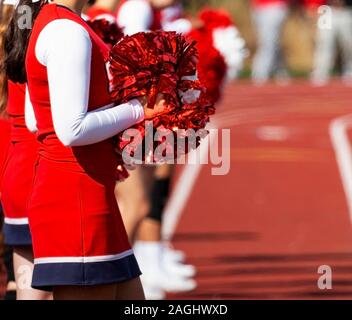 Sonnenlicht spiegelt sich der rote Bommeln, Cheerleadern halten beim Stehen auf einer Spur einen High School Football Spiel. Stockfoto