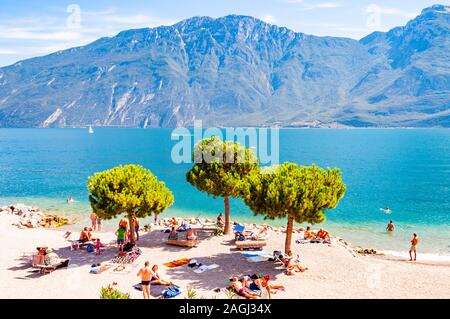 In Limone am Gardasee, Lombardei, Italien - 12 September 2019: Cosy Beach auf der westlichen Küste des Sees. Menschen schwimmen Sonnen am Ufer unter hohem Ev Stockfoto