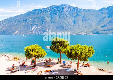 In Limone am Gardasee, Lombardei, Italien - 12 September 2019: Cosy Beach auf der westlichen Küste des Sees. Menschen schwimmen Sonnen am Ufer unter hohem Ev Stockfoto