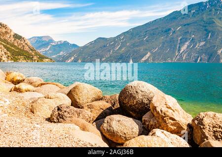 Runde Felsen liegen am Ufer des wunderschönen Gardasee, Lombardei, Italien von hohen Bergen der Dolomiten umgeben. Single Classic weiß Segelyacht Stockfoto