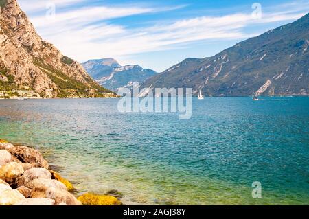 Runde Felsen liegen am Ufer des wunderschönen Gardasee, Lombardei, Italien von hohen Bergen der Dolomiten umgeben. Classic weiß Segelyacht floati Stockfoto