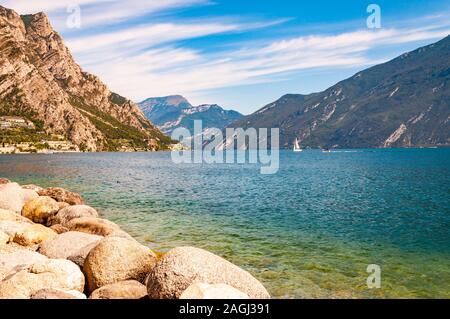 Runde Felsen liegen am Ufer des wunderschönen Gardasee, Lombardei, Italien von hohen Bergen der Dolomiten umgeben. Classic weiß Segelyacht floati Stockfoto