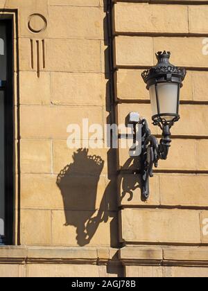 Aufwändige schwarzen schmiedeeisernen Straßenlaterne und Halterung wirft einen Schatten auf die Diagonale parallel Kurse von Gekleideten Steinmauer in San Sebastian, Spanien, Europa Stockfoto