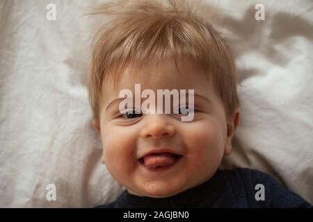 Nahaufnahme von Happy Cute Baby Gesicht mit großen braunen Augen, lange Wimpern und blondes Haar klebt seine Zunge aus seinem Mund, während zu lächeln und zu lachen. Stockfoto