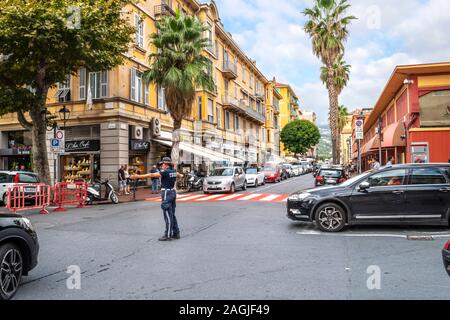 Eine weibliche Polizistin leitet Datenverkehr an einem roten und weißen Zebrastreifen in das städtische Zentrum von Ventimiglia an der italienischen Riviera. Stockfoto