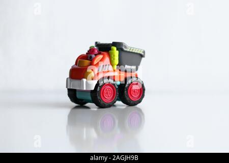 Kunststoff Dump Truck Spielzeug Bau fahrzeug auf weißem Hintergrund mit Reflexion isoliert. Dumper Seite anzeigen. Orange Fahrzeug mit roten Räder und Name Text. Operator in roten Schutzhelm Stockfoto