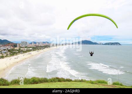 Luftaufnahme der Cove Beach in Guaruja SP Brasilien. Gleitschirm fliegen über dem Meer, am Strand, Meer, Wellen und der Stadt im Hintergrund Stockfoto