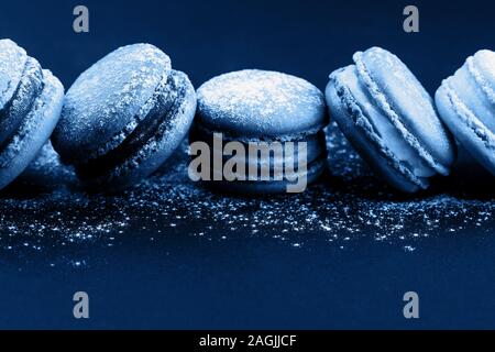 Zeile der französischen Makronen mit Puderzucker, liegen auf schwarzen Hintergrund in blauer Farbe. Stockfoto