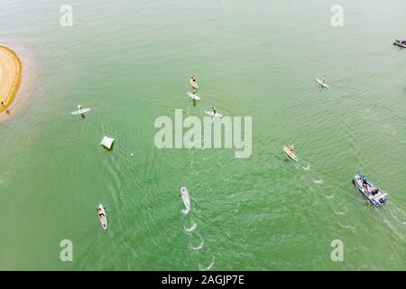 Starke Männer, die an einem sonnigen Tag auf einem SUP-Brett in einer wunderschönen Bucht schweben. Luftaufnahme der Männer überquert die Bucht mit dem Paddleboard. Wassersport Stockfoto