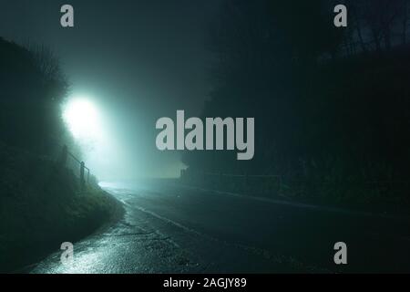 Eine gruselige, schaurige Country Road, die durch einen Hügel. Auf einer geheimnisvollen Nebel, winter nacht. Stockfoto