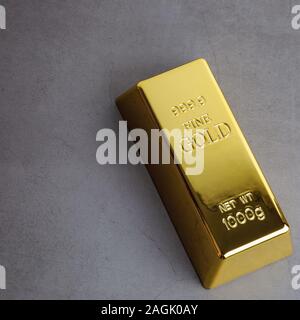 Ein Barren aus Gold Metal bullion der reinen Brillanten schräg auf einem grauen strukturierten Hintergrund entfernt Stockfoto