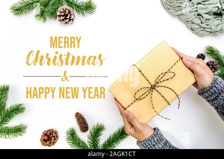 Weihnachten Winter Zusammensetzung. Frau Hand halten Weihnachten Geschenk Box mit Tannenzapfen, tannenzweigen auf weißem Hintergrund. Flach, Ansicht von oben, kopieren Raum Stockfoto