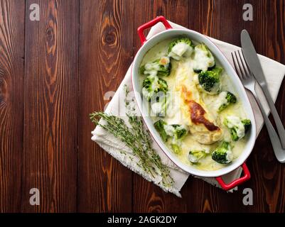 Hähnchenbrustfilet überbacken mit Broccoli in bechamelsauce Soße auf einem dunklen Holztisch. Gesunde Nahrung, sauberes Essen, Ansicht von oben, kopieren Raum Stockfoto