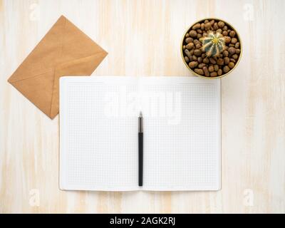Öffnen Sie Notepad, weiß Kraftpapier Umschlag und Kaktus im Topf liegen auf einem beige Schreibtisch aus Holz, Flach, Copyspace Stockfoto