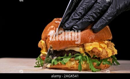 Schneiden Handwerk Burger ist Kochen auf schwarzem Hintergrund. Bestehen: sauce, Rucola, Tomaten, roten Zwiebeln Pommes, Gurken, Käse, Brötchen und Fleisch. Stockfoto