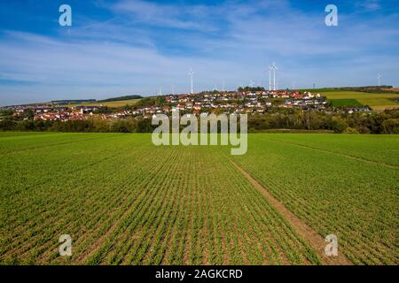 Windkraftanlagen hinter einer landwirtschaftlichen Feld und das Dorf, zwischen Feldern, auf dem Abhang eines Hügels Stockfoto