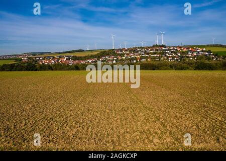 Windkraftanlagen hinter einer landwirtschaftlichen Feld und das Dorf, zwischen Feldern, auf dem Abhang eines Hügels Stockfoto