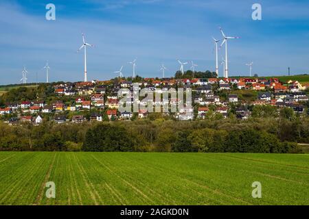 Windkraftanlagen hinter einer landwirtschaftlichen Feld und das Dorf, zwischen Feldern, auf dem Abhang eines Hügels Stockfoto