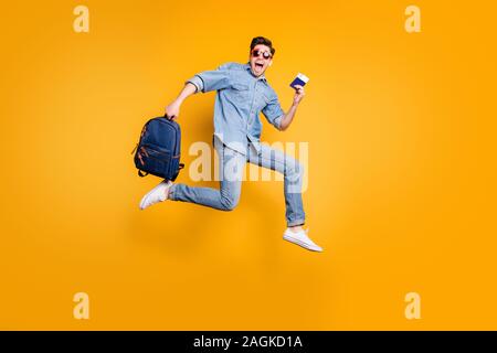 Volle Länge Körper Größe gedreht Foto von schreienden Mann laufen Springen in Richtung Flughafen in weiße Schuhe und Tasche in der Hand isoliert leuchtend gelben Farbe Stockfoto