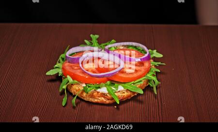 Handwerk Burger ist Kochen auf schwarzem Hintergrund. Bestehen: sauce, Rucola, Tomaten, Zwiebeln, Speck, Johannisbeeren Sauce, ricotta Käse, Brötchen und Fleisch. Stockfoto