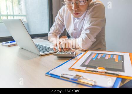 Junger Mann mit Taschenrechner arbeiten an finanziellen Unterlagen und Laptop Stockfoto