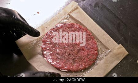 Kochen macht Fleisch Medaillons für Burger. Koch in schwarz Handschuhe macht Schnitzel essen. Die koteletts sind in Stahl Ring in eine noch Medaillon eingeebnet. Stockfoto
