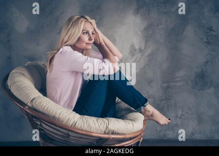 Full Body Profil Seite Foto von Verträumten gleichgesinnten Frau mittleren Alters sitzen in wicker moderne Sessel Traum über freie Zeit vorstellen, Urlaub in Zimmer Haus Stockfoto