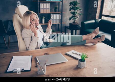 Foto fröhliche, schöne charmante positive Assistant am Telefon sprechen am Ende des Arbeitstages Ihre Brillen, weg von der mit den Beinen auf dem Tisch Stockfoto