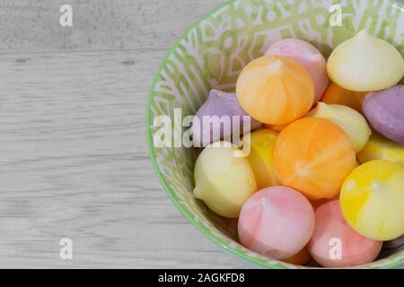 Baisers, verschiedene Farben, in einem grün gemusterten Schüssel Schüssel. Graues Holz Hintergrund Stockfoto